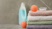 Dryer balls, detergents and stacked clean towels on grey marble table. Space for text