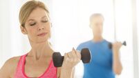 Mature woman lifting dumbbell with man in background at home