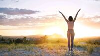 Young girl with open arms freely at mountain top against sunset.