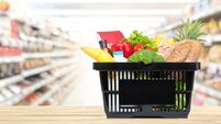Food and groceries in shopping basket on wood table with blurred suppermarket aisle in background
