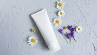 Mock-up of white squeeze bottle cosmetic tube, Chamomiles flowers on gray table. Natural organic spa cosmetics concept. Top view