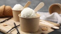 Paper cups with delicious ice cream and vanilla pods on wooden board, closeup