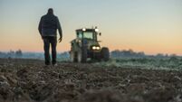 Male farmer with short brown hair,walking in the direction to his tractor,standing next to his agricultural field in the evening