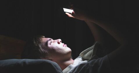 Depressed teenager on his phone in the dark.