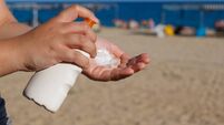 Woman hands applying sunscreen, with the beach in the background